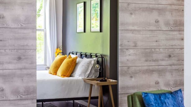 Un dormitorio con cama, mesita de noche, silla y ventana.