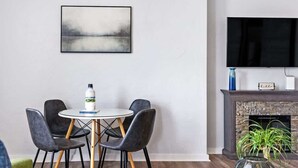 Una sala de estar moderna con una mesa redonda de comedor, cuatro sillas, un televisor de pantalla plana, una chimenea y un cuadro en la pared.
