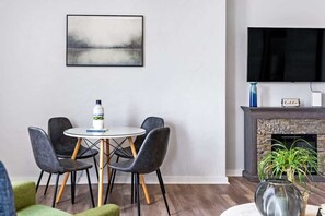 A modern living room with a round dining table, four chairs, a flat-screen TV, a fireplace, and a painting on the wall. - Hot Tub | King Bed | Free Parking |  Pac-Man (Pittsburgh)