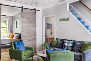 A living room with a sofa, chairs, a coffee table, a staircase, and a door with a sign. - Hot Tub | King Bed | Free Parking |  Pac-Man (Pittsburgh)
