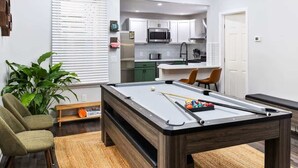 A pool table in a room with a kitchen in the background, a plant, and a chair. - 2 King Beds w Hot Tub Near Butler St (Pittsburgh)