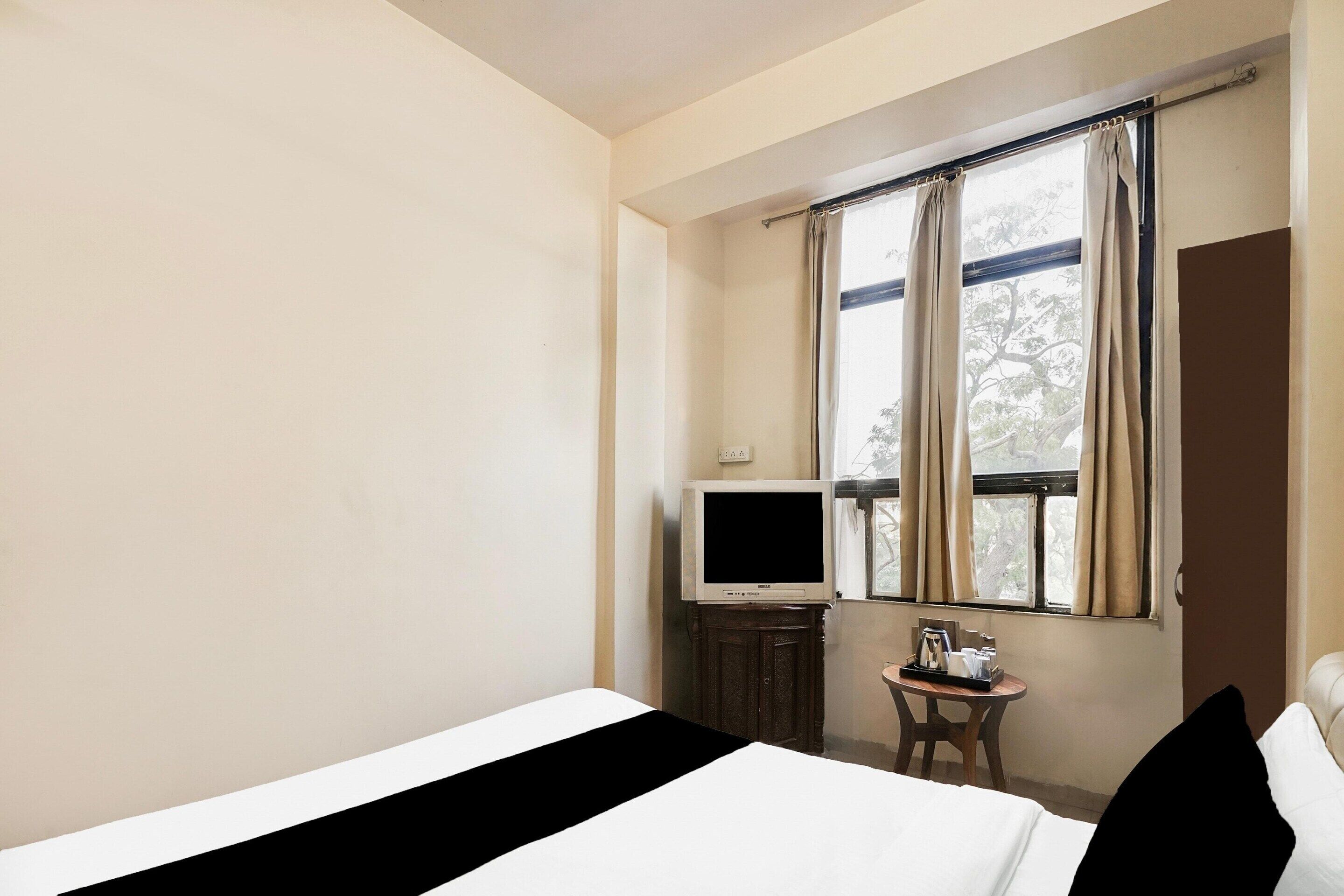 Hotelkamer met een bed, een televisie, een klein tafeltje met dienblad en een raam met gordijnen.