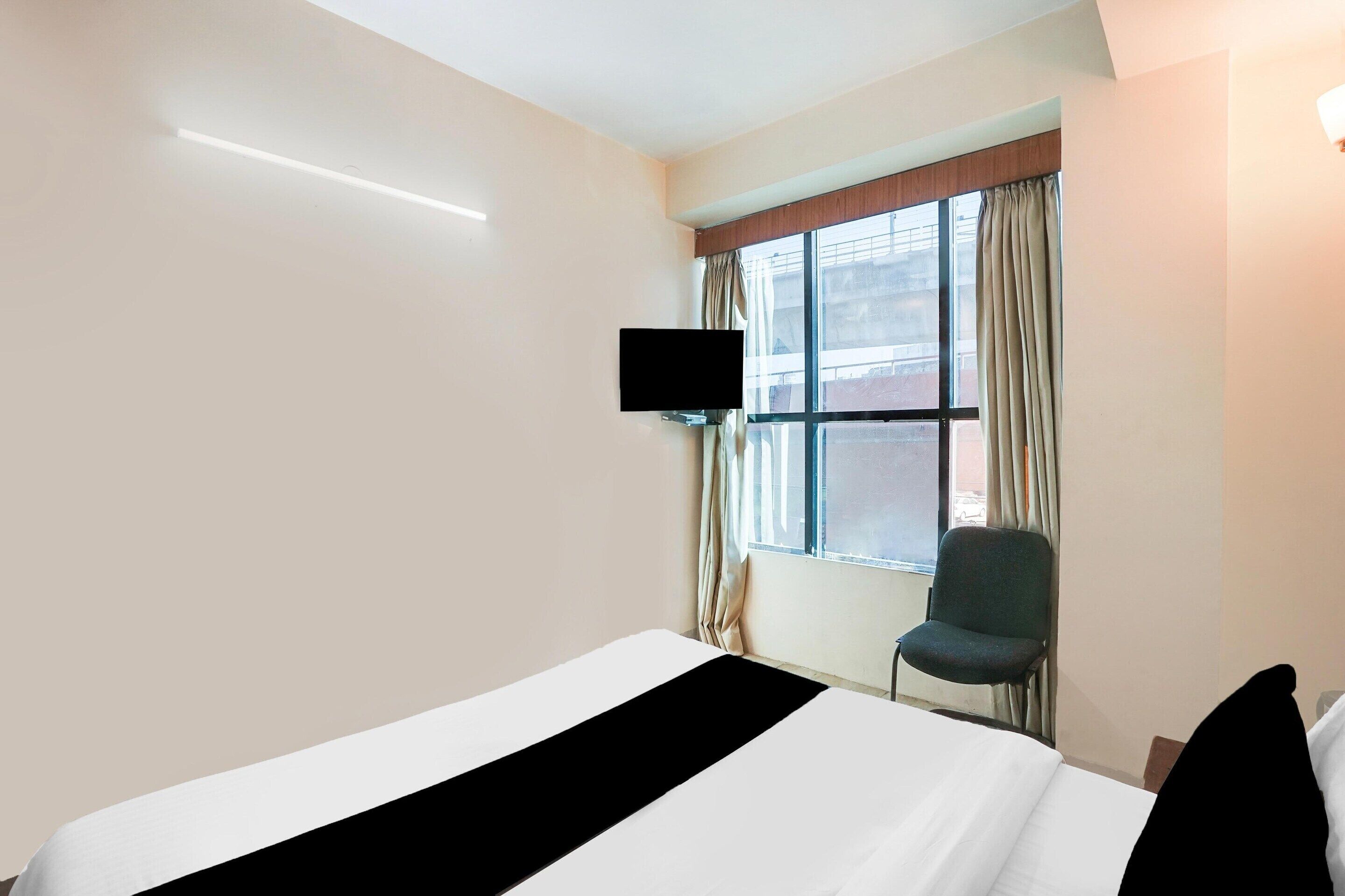 A hotel room with a bed, a television mounted on the wall, a chair, and a window with curtains.