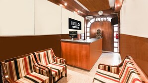Ein Hotel-Empfangsbereich mit gestreiften Stühlen, einem Empfangstresen, einer Uhr und einem Fernseher.