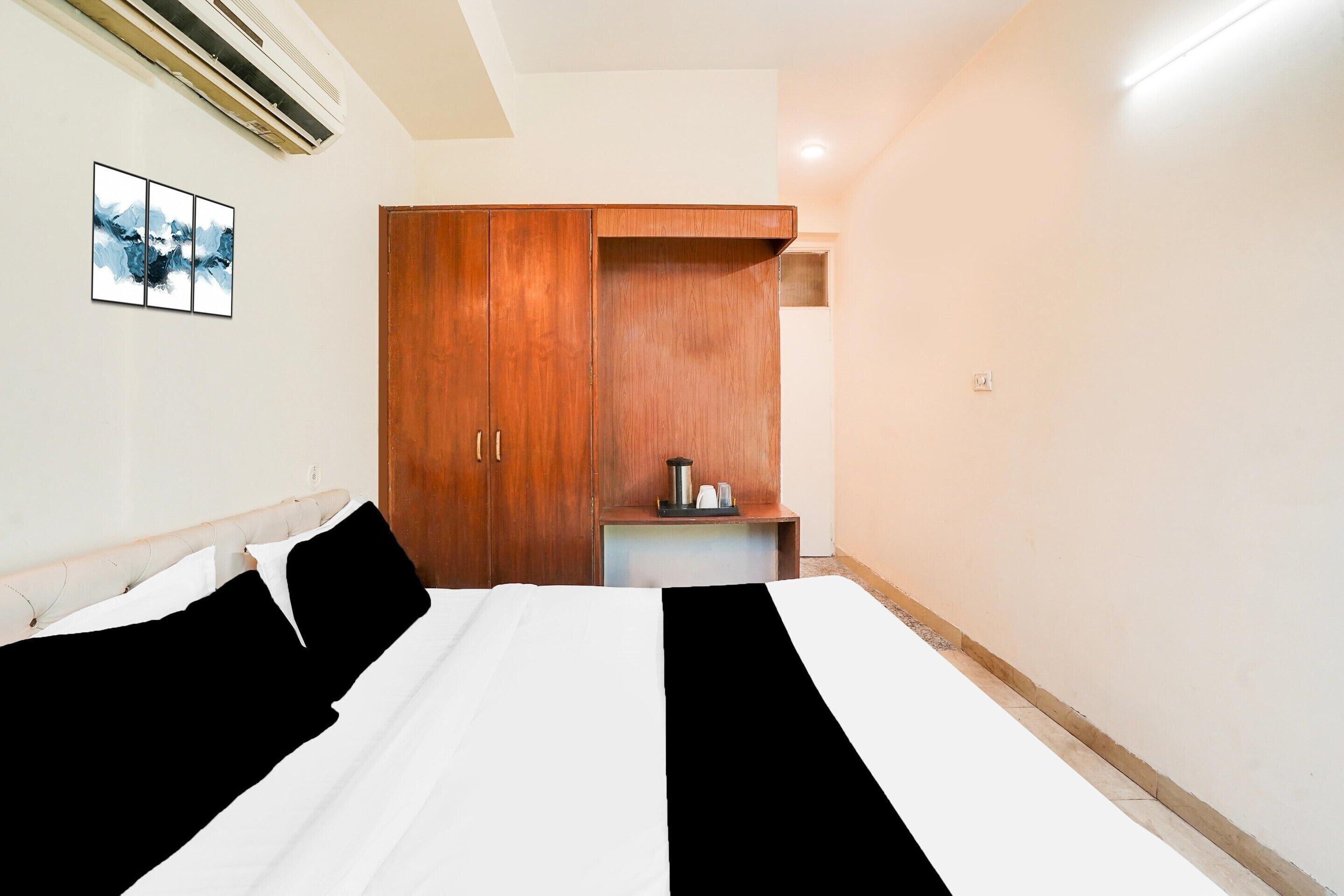 Habitación de hotel con cama, armario de madera, una mesita con hervidor y aire acondicionado instalado en la pared.