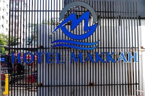 Segnaletica di un hotel con un logo e la scritta 'HOTEL MAKKAH' su un cancello in metallo.
