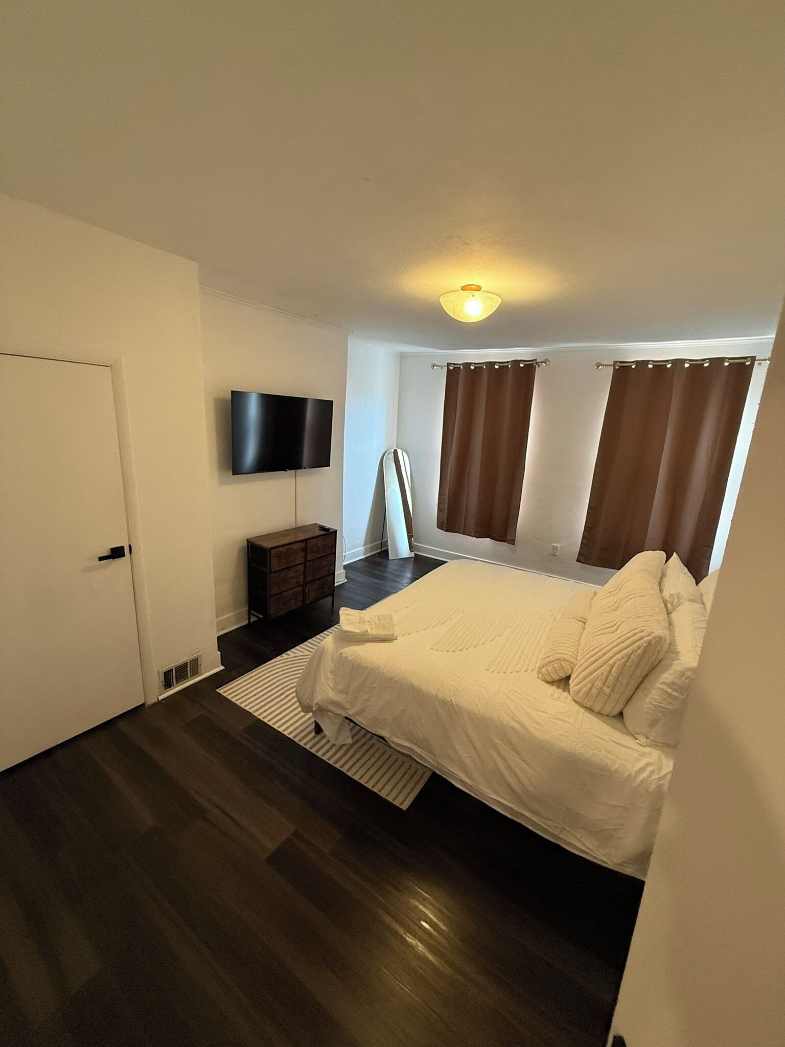 A bedroom with a bed, a flat-screen TV, a dresser, and a window with curtains.