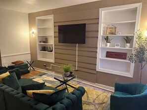 Una sala de estar con una televisión de pantalla plana montada en la pared, un sofá, una mesa de centro y dos mesitas de noche.