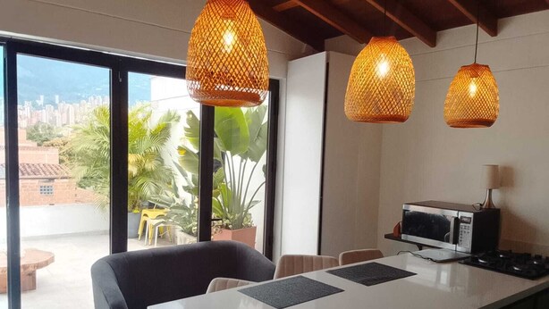 A modern kitchen with a large island, pendant lights, and a view of a cityscape through large windows. - Serene 2-bedroom apartment in Medellín perfect for your getaway . Amaizing view (barrio santa fe medellin)