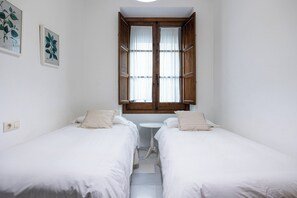 Ett litet, rent rum med två enkelsängar, ett litet bord och ett fönster med gardiner.