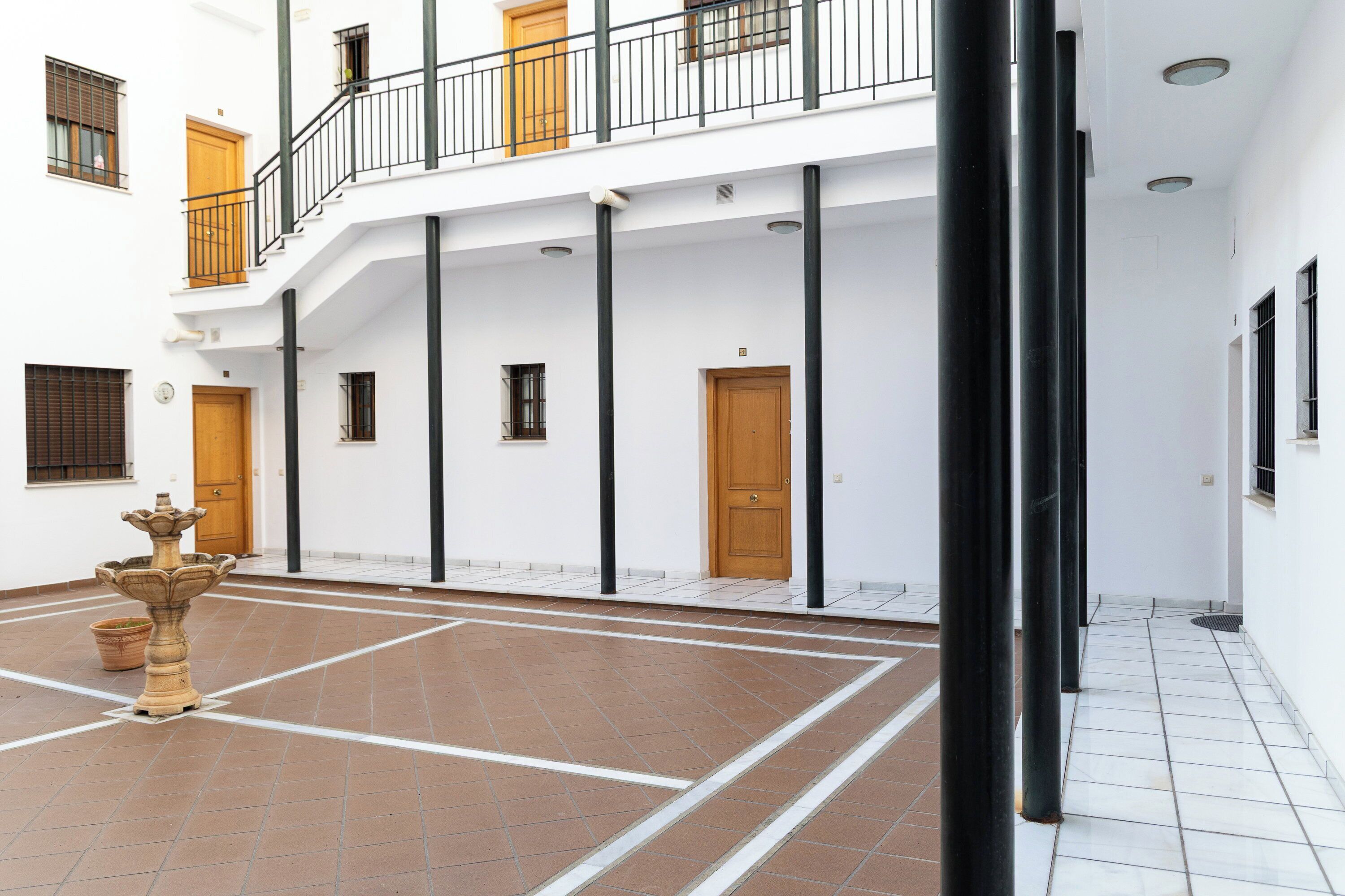 Un cortile con una fontana, pavimento piastrellato e un edificio con diverse porte e finestre.