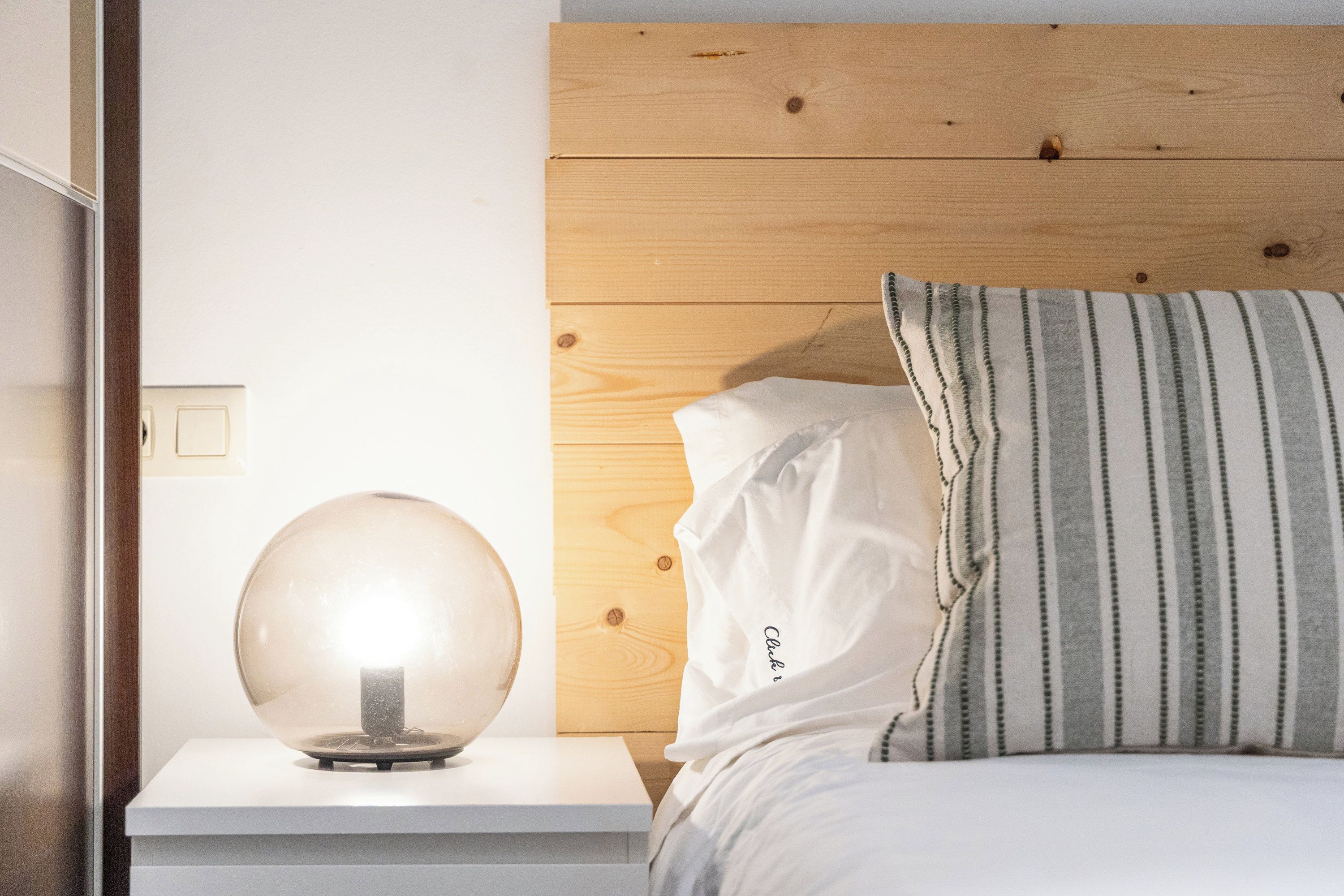 A bed with a wooden headboard, a bedside lamp, and a striped pillow.