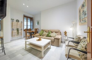 Een woonkamer met een bank, een salontafel, een eettafel met stoelen en een raam met gordijnen.