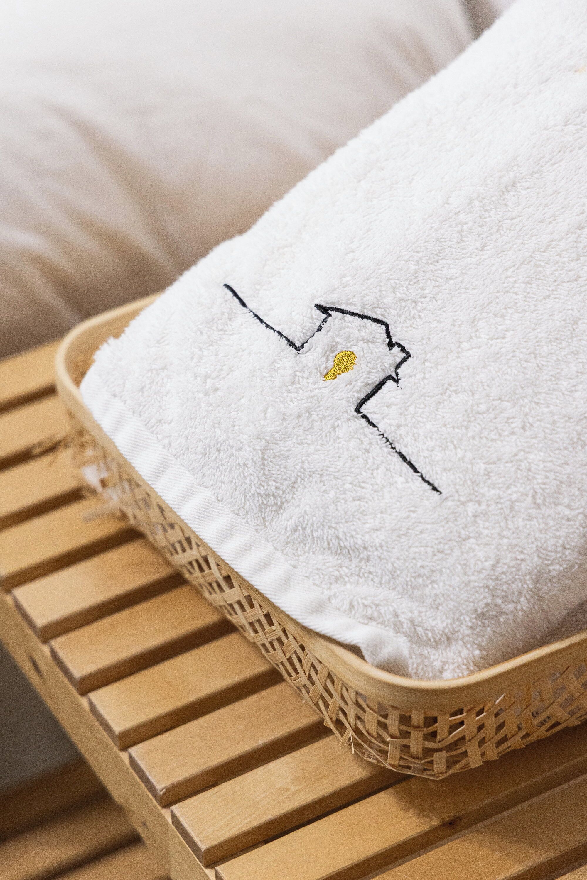 A white towel with a black and yellow embroidered design, placed on a woven basket.