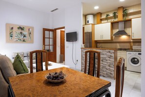 A modern kitchen with a built-in washer and dryer, wooden cabinets, and a dining area with a table and chairs. - Córdoba Center Monumental Home (Cordoba)
