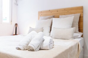 Cama bem arrumada com lençóis e almofadas brancos, cabeceira de madeira e mesa de cabeceira com abajur.