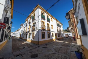 A building with multiple floors, balconies, and a cobblestone street. - Cozy Retreat with Patio Steps from Alcázar (Cordoba)