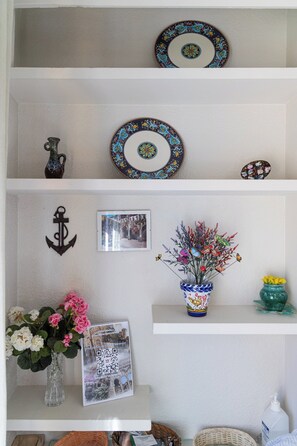 Uma prateleira com pratos decorativos, um vaso com flores, uma fotografia emoldurada e um código QR.