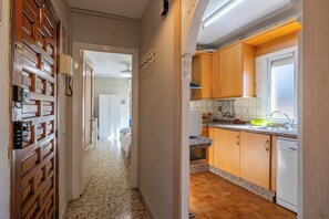 Un couloir mène à une cuisine équipée de meubles de rangement en bois, d’un plan de travail et d’un lave-vaisselle.