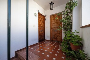 Ein Flur mit zwei Holztüren, Fliesenboden, einem Blumentopf und einer Wandleuchte.