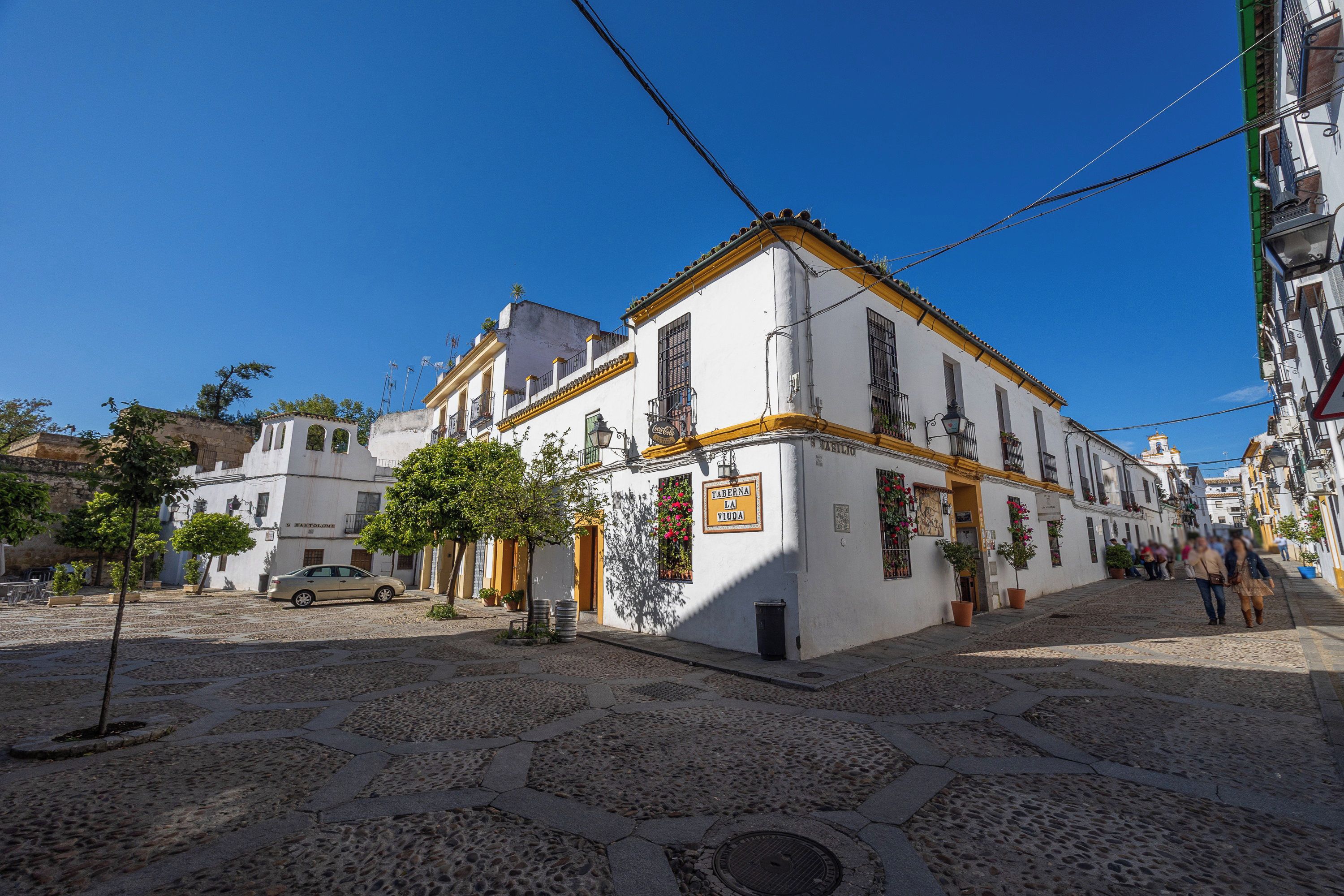 A cobblestone street with a white building featuring a sign for 'Taberna La Viuda'.