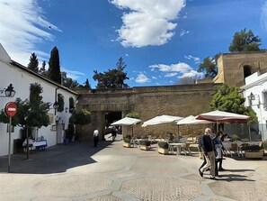 An outdoor courtyard with stone flooring, outdoor seating, and a building with a brick facade. - Cozy Retreat with Patio Steps from Alcázar (Cordoba)