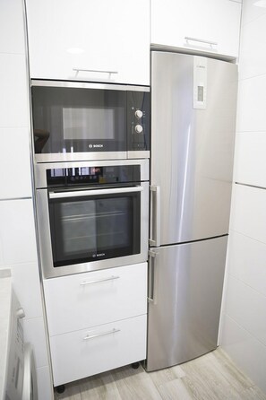 Una cocina con horno y refrigerador Bosch de acero inoxidable, armarios empotrados blancos y salpicadero de azulejos.