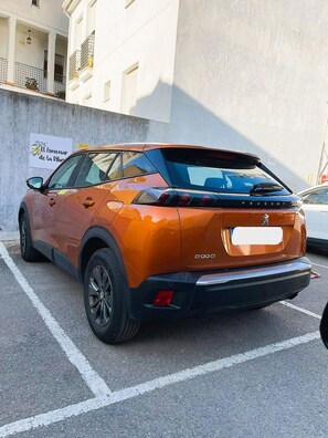 Un SUV naranja estacionado en un estacionamiento, con un edificio al fondo.