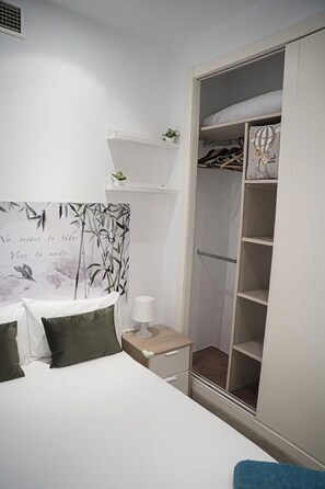 Un dormitorio con cama, mesita de noche, lámpara y armario con estantes.