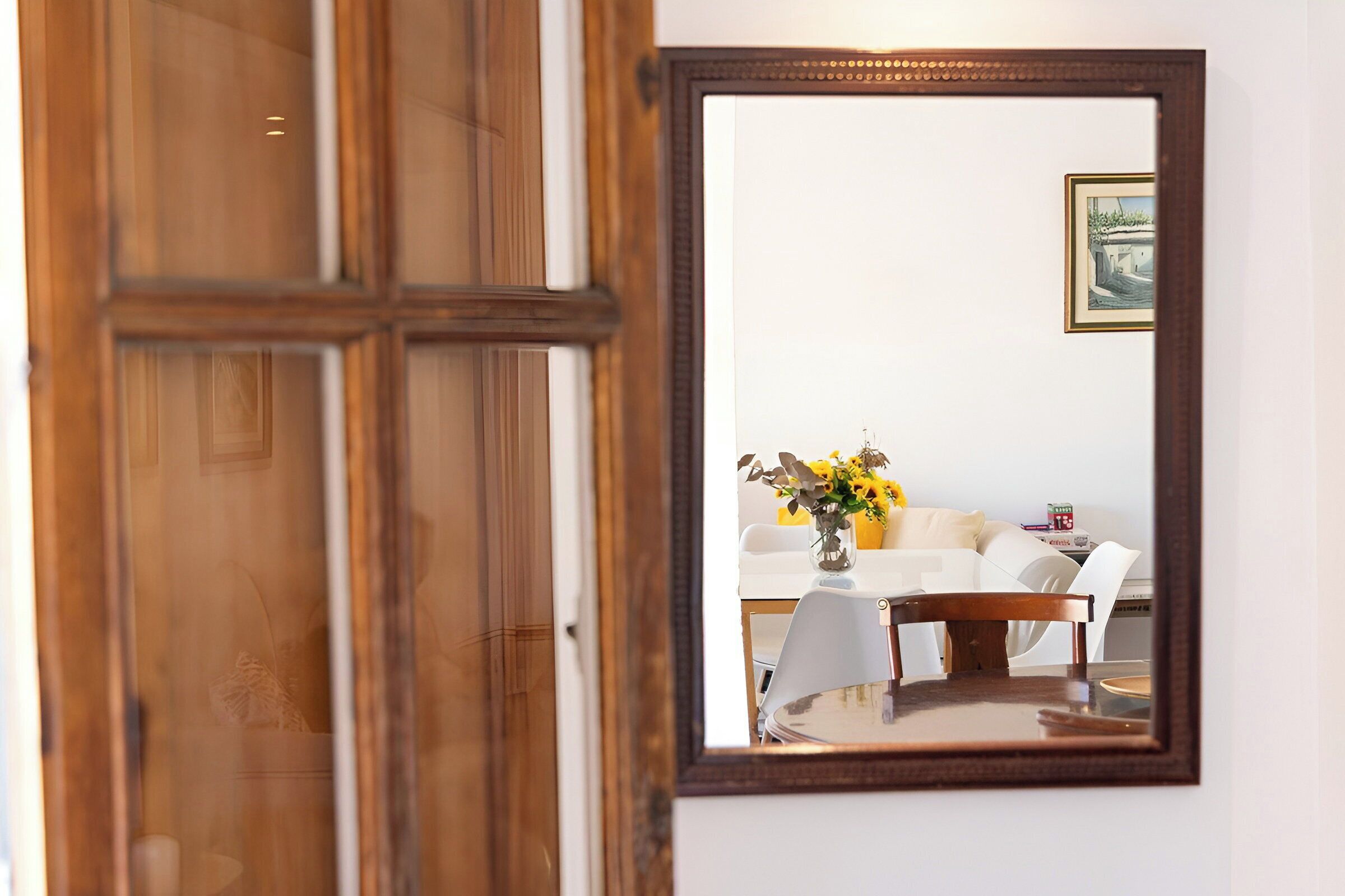 Ein Zimmer mit Holztür, einem Esstisch mit Stühlen und einer Vase mit Blumen.