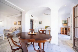 Ein Essbereich mit einem runden Holztisch, Stühlen, einem weißen Sofa und einem Bücherregal im Hintergrund.