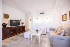 Ein Wohnzimmer mit Fernseher, einem weißen Sofa, einem weißen Sessel und einem Couchtisch.