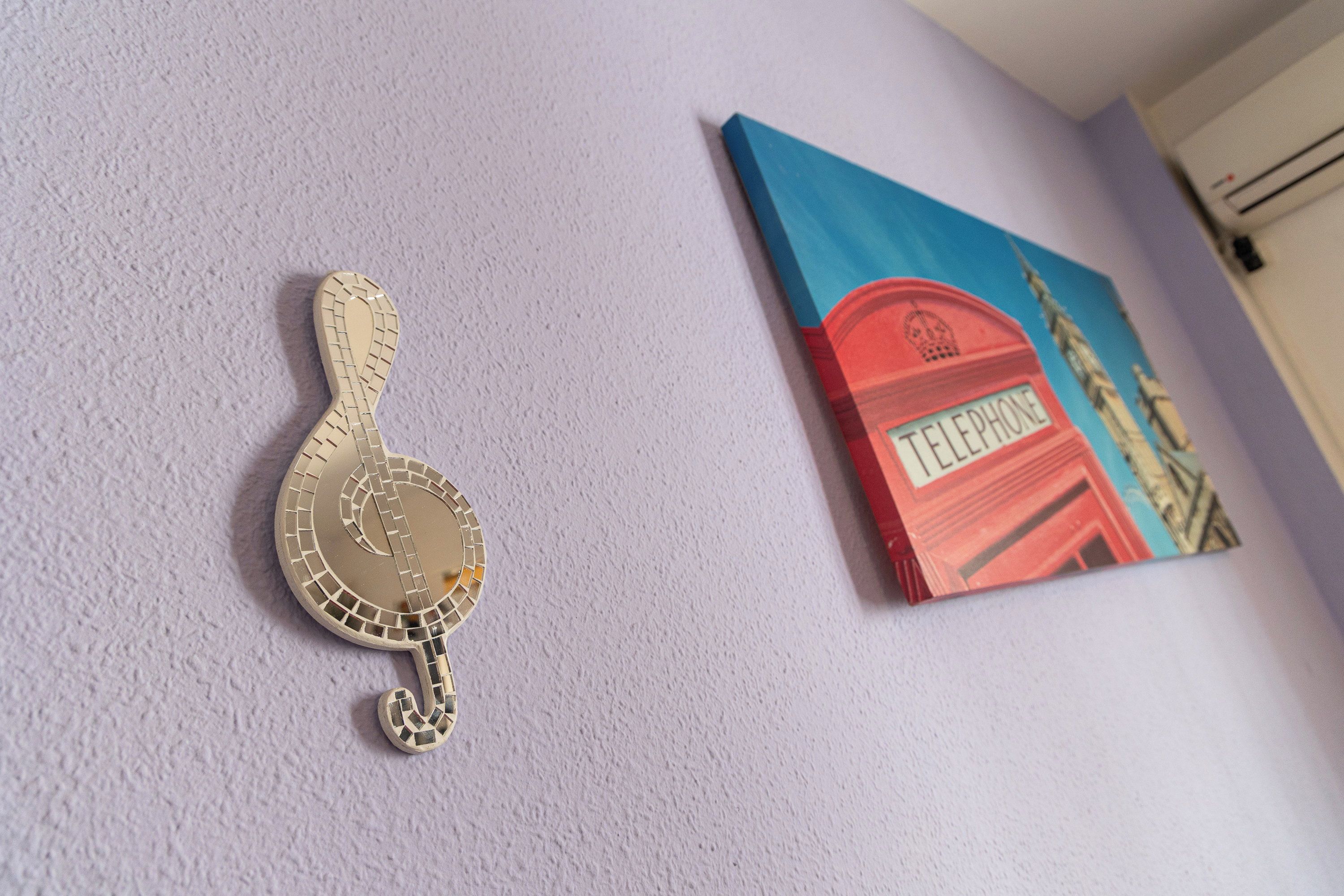 A wall with a decorative item resembling a musical instrument and a framed artwork depicting a red telephone booth.