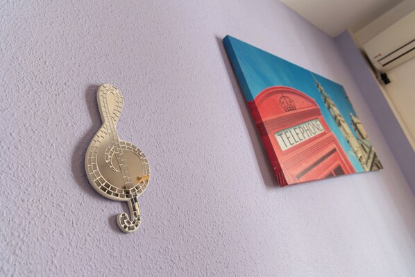 Eine Wand mit einem dekorativen Gegenstand, der ein Musikinstrument ähnelt, und einem gerahmten Kunstwerk, das eine rote Telefonzelle zeigt.