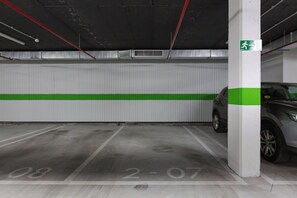 Eine Parkgarage mit weiß-grün gestreiftem Mauerwerk, ein graues Auto parkiert und ein grünes Notausgangsschild.