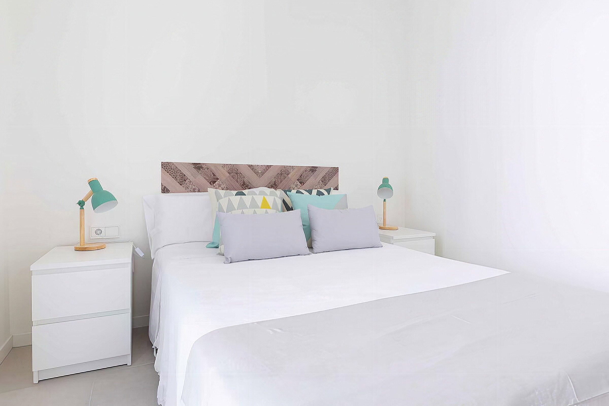 Een witte slaapkamer met een bed, twee nachtkastjes en een vastgezet hoofdbord.