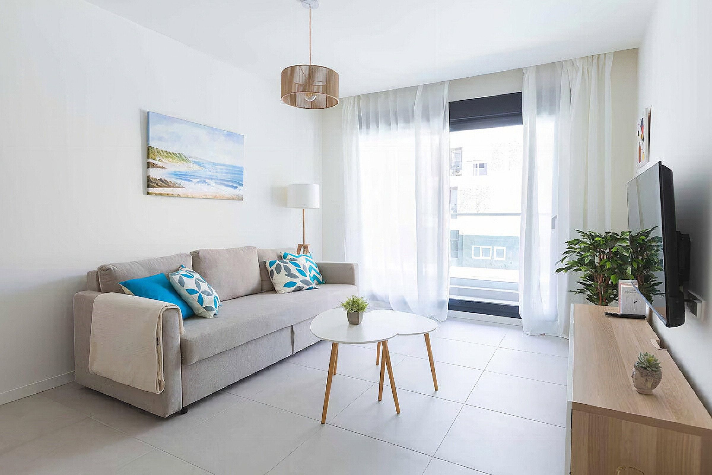 A modern living room with a sofa, a small round table, a lamp, a TV, and a window with curtains.