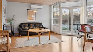 A modern living room with a leather sofa, a round wooden table, and a glass door leading outside. - 4 Star Holiday Home in Vig (Vig)