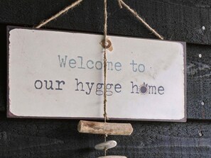 Ein rustikales Willkommensschild mit dem Schriftzug 'Welcome to our hygiene home' an einer dunklen, strukturierten Wand.