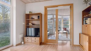 A modern living room with wooden flooring, a built-in TV, and a sliding glass door leading to an outdoor area. - 4 Star Holiday Home in Vig (Vig)