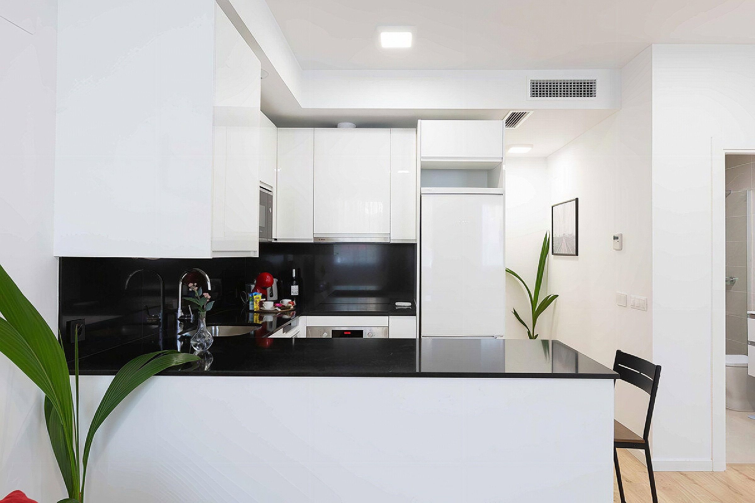 A modern kitchen with white cabinetry, a black countertop, and a dining area with a chair.
