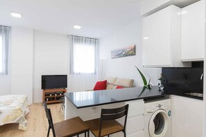 A modern kitchen with a central island, a flat-screen TV, a washing machine, and a dining area with a table and chairs. - Cosmopolitan Loft & Malaga Beach (Málaga)