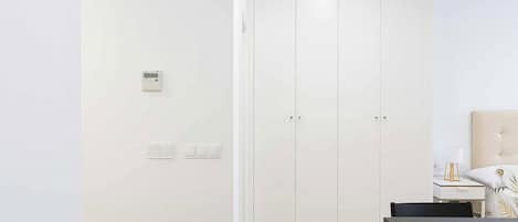 A minimalist room with a white door, a small bedside table with a lamp, and a wooden floor.