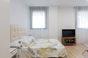 A hotel room with a bed, a television on a wooden stand, and two windows with sheer curtains. - Cosmopolitan Loft & Malaga Beach (Málaga)