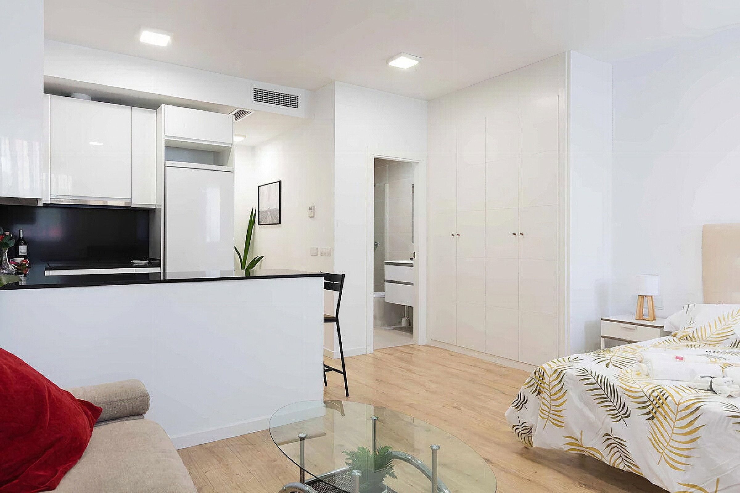 Un appartement moderne comprenant un coin cuisine, un espace repas, un salon avec une table basse en verre et une chambre à coucher avec un lit et une table de chevet.
