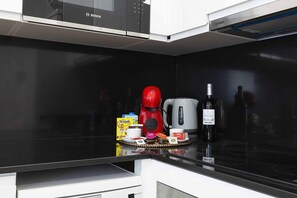 A kitchen with a black countertop, a red coffee maker, a white kettle, a bottle of wine, and a box of Nescafé. - Cosmopolitan Loft & Malaga Beach (Málaga)