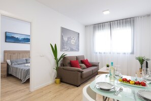 A modern living room with a sofa, a dining table set for two, and a large window with curtains. - Cosmopolitan Apt & Malaga Beach (Málaga)