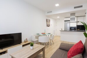 A modern living room with a flat-screen TV, a dining table with chairs, a kitchen area with a stove and microwave, and a red cushion on a sofa. - Cosmopolitan Apt & Malaga Beach (Málaga)
