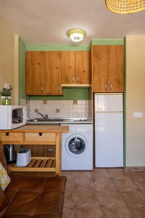 Eine kompakte Küche mit Holzschränken, einer Waschmaschine, einer Mikrowelle und einem Kühlschrank.