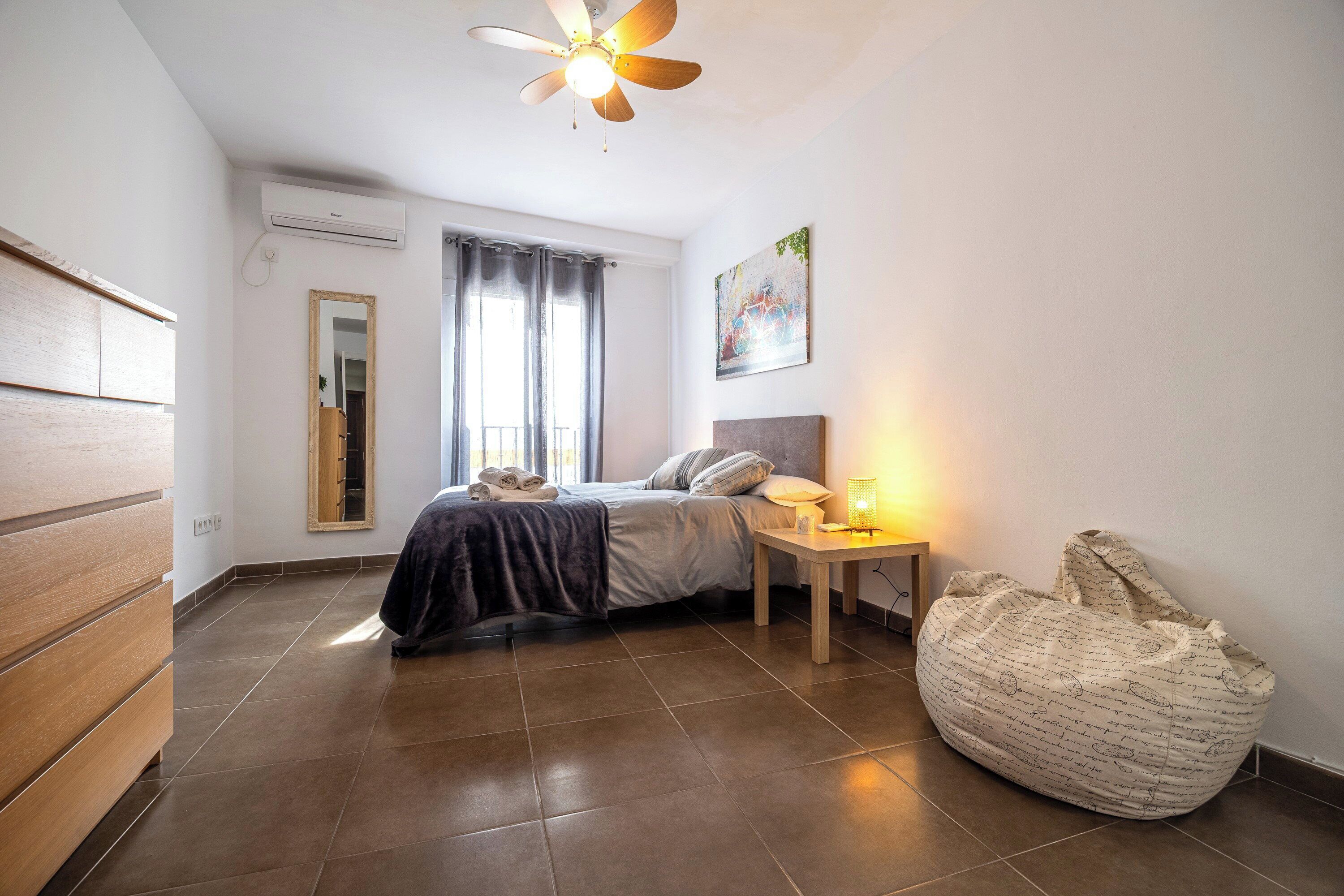A bedroom with a bed, bedside table, lamp, and a chair.